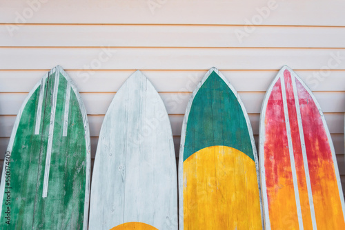 Several surfboards of different colorful saturated yellow, green, red colors lined up against the wall.