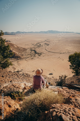 Touristin sitzt auf einem Felsen unterhalb eines Gipfels am Rande der Aus-Berge und blickt in die Weite der Namib (Klein-Aus Vista, Namibia) photo