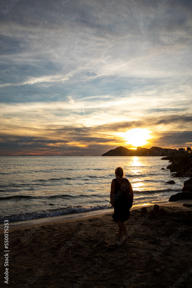 Mujer solitaria reflexionando sobre el amor en un día muy especial mientras observa el atardecer a la orilla del tranquilo mar.