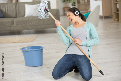 happy young cleaning woman using mop as guitar