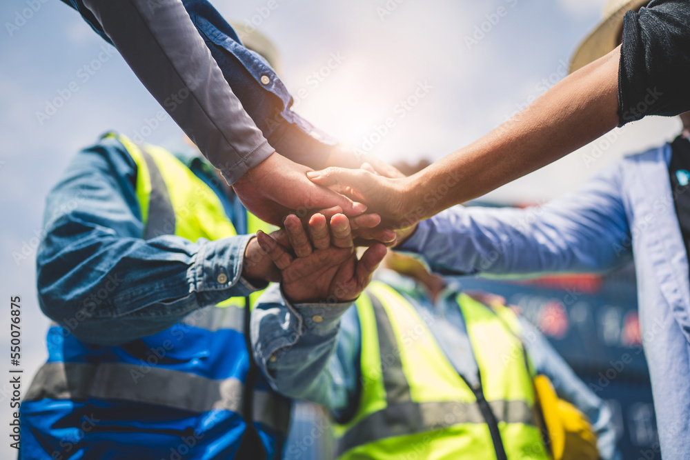 Close-up of Engineering team making pile of hands with cargo container background at sunset. Logistics global import or export shipping industrial concept. Close-up of Engineering team making pile of hands with cargo container background at sunset. Logistics global import or export shipping industrial concept.