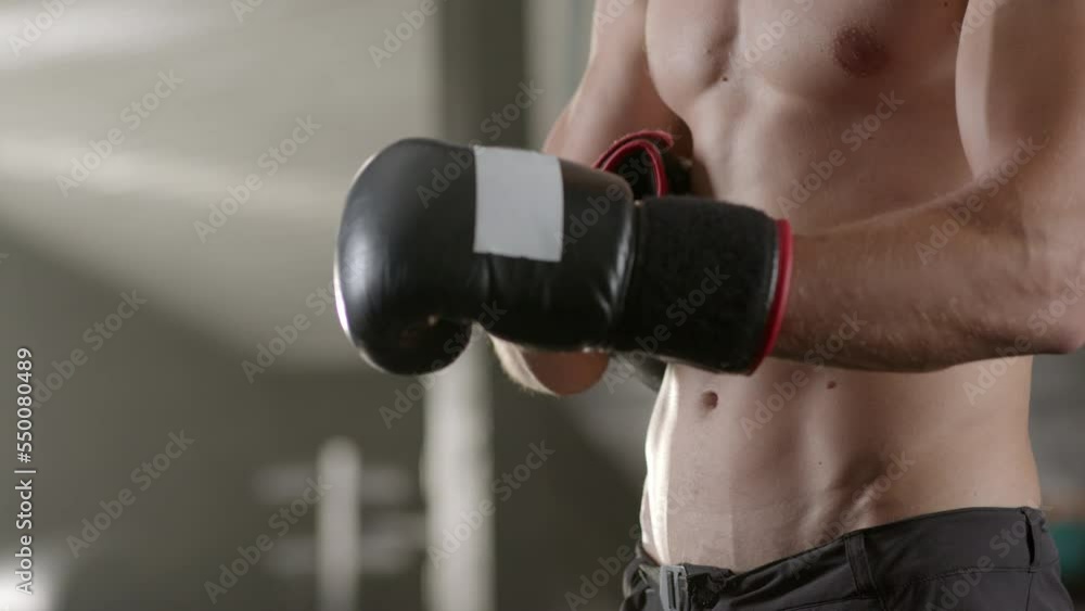 Close-up portrait shot of male boxer wearing boxing gloves in dark gym. Sports Training. Slow-motion Close-up portrait shot of male boxer wearing boxing gloves in dark gym. Sports Training. Slow-motion