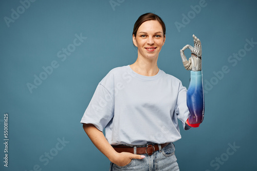 Cheerful young woman with bionic arm showing ok sign, isolated on greyish blu photo