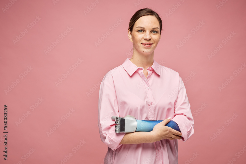 Portrait of smiling young woman with bionic arm standing against pink background Portrait of smiling young woman with bionic arm standing against pink background