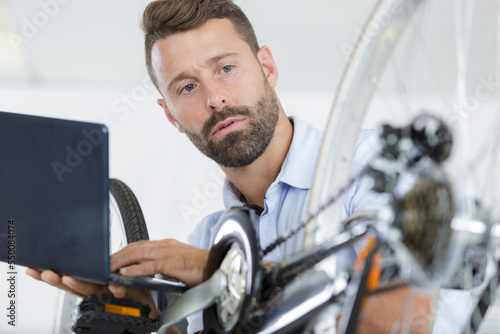 man checking his laptop while repairing bicycle at home