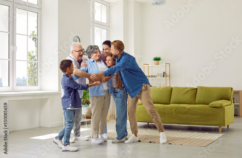 Happy large cute family hugging their beloved grandmother in a cozy bright spacious room at home. Concept of a dynasty in three generations, family ties, unconditional love, family relations, reunion. © Studio Romantic