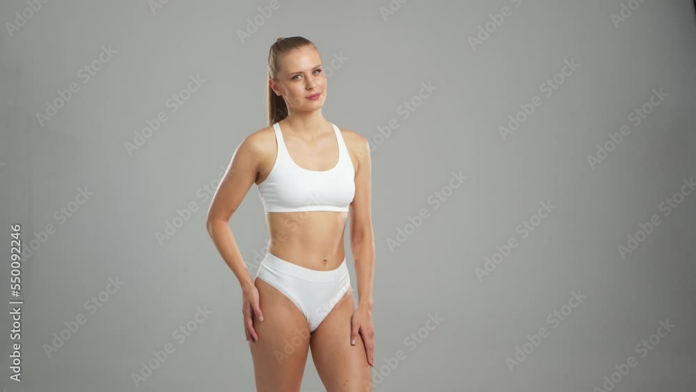 Young, fit and beautiful blond woman in white swimsuit posing over grey background. Healthcare, diet, sport and fitness concept. Young, fit and beautiful blond woman in white swimsuit posing over grey background. Healthcare, diet, sport and fitness concept.