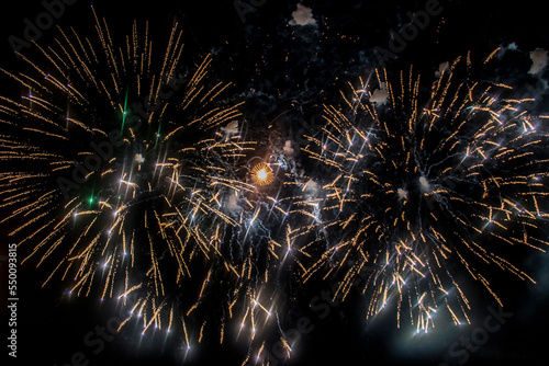 beige and yellow fireworks burst into various shapes in the dark sky during the holiday