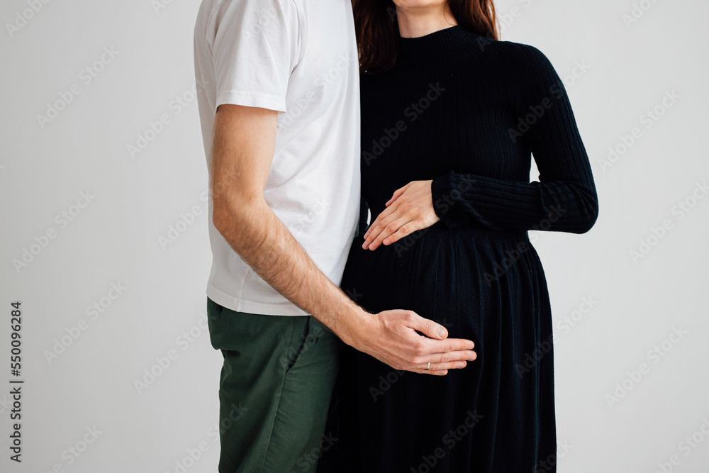 young couple family a man in a white T-shirt hugs the belly of his pregnant partner woman wife in a black dress, hands on the stomach close-up