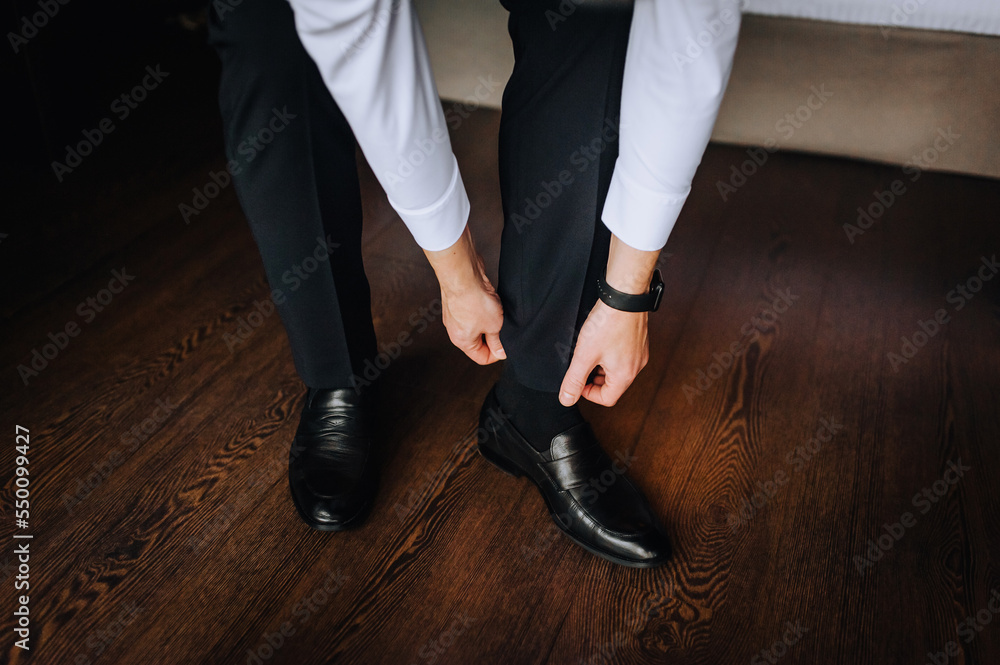 Man, groom, businessman getting ready in the morning, putting on black leather shoes on his foot. Wedding photography, business.