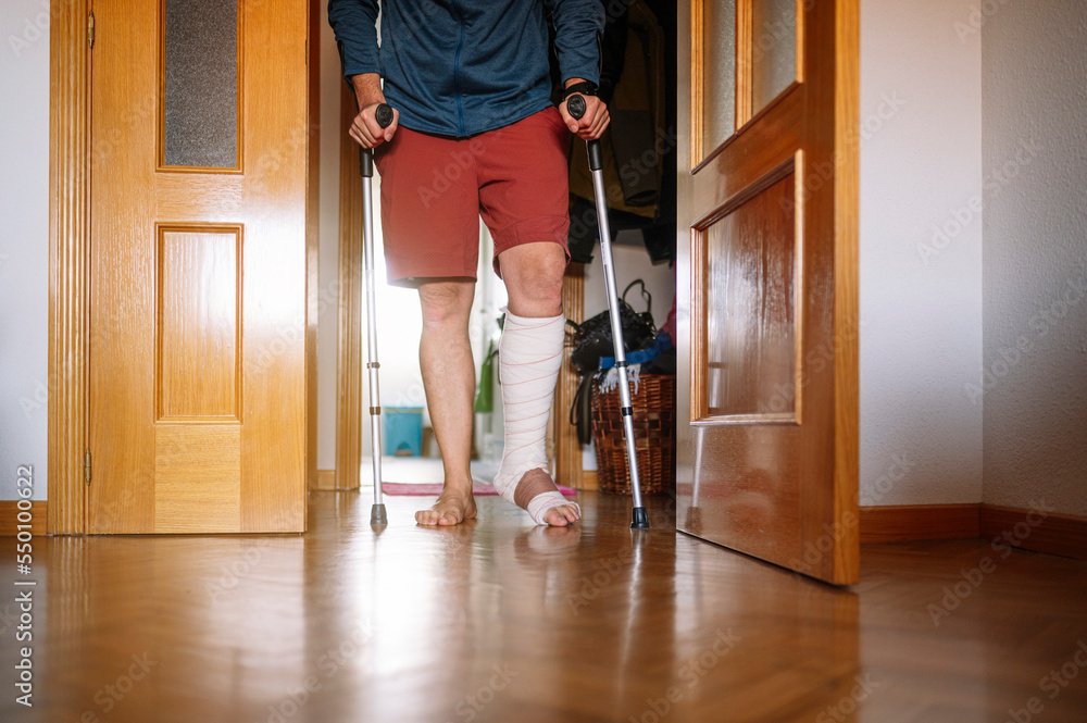 Injured man with bandaged foot walking at home with walking sticks. Injured man with bandaged foot walking at home with walking sticks.