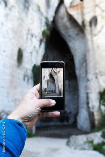 Tourist photographing entrance of Orecchio di Dionisio cavern, Neapolis, Siracusa, Sicily, Italy photo
