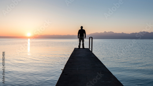 Lonely man standing on pier by Geneva Lake, at sunrise in summer, Gland, Vaud, Switzerland photo