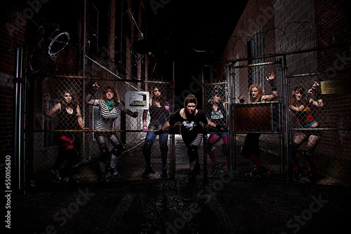 A women's roller derby team outfitted in the full roller derby fashion style glares out from behind a fence in a dark alley in New Haven, Connecticut. photo