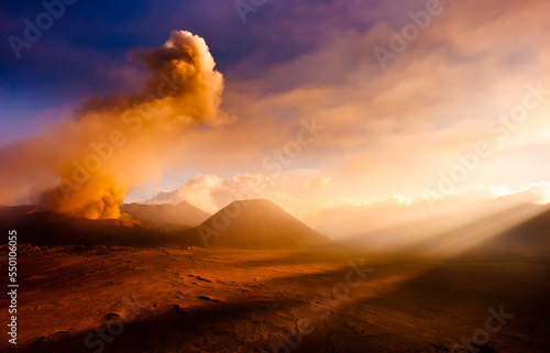 Mt. Bromo volcano erupting with strong god rays in the foreground.
