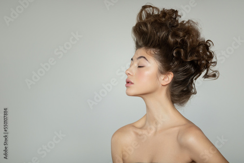 Portrait of a beautiful brown-haired woman with a curly haircut. Gray background.