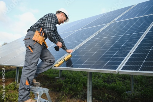 Professional worker installing solar panels on the metal construction, using different equipment, wearing helmet. Innovative solution for energy solving. Use renewable resources. Green energy. © Serhii