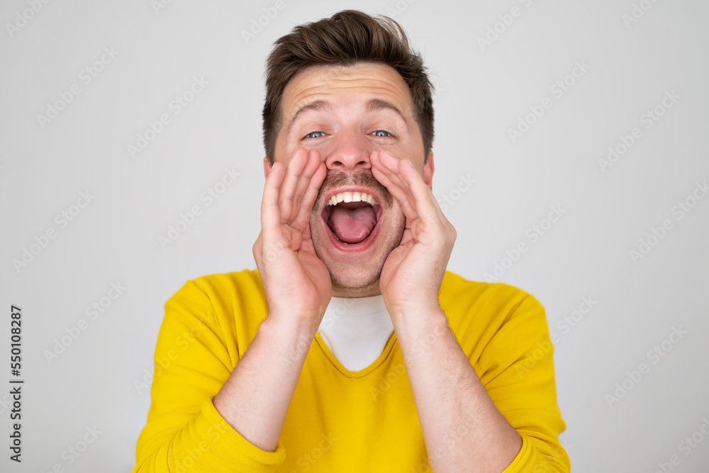Excited young caucasian man shouting with hands cupped around mouth Excited young caucasian man shouting with hands cupped around mouth