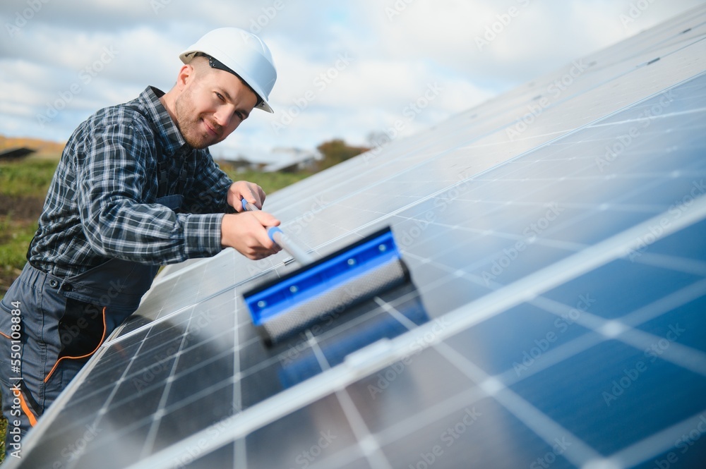 technician operating and cleaning solar panels at generating power of solar power plant; technician in industry uniform on level of job description at industrial technician operating and cleaning solar panels at generating power of solar power plant; technician in industry uniform on level of job description at industrial