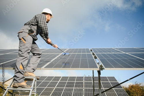 technician operating and cleaning solar panels at generating power of solar power plant; technician in industry uniform on level of job description at industrial