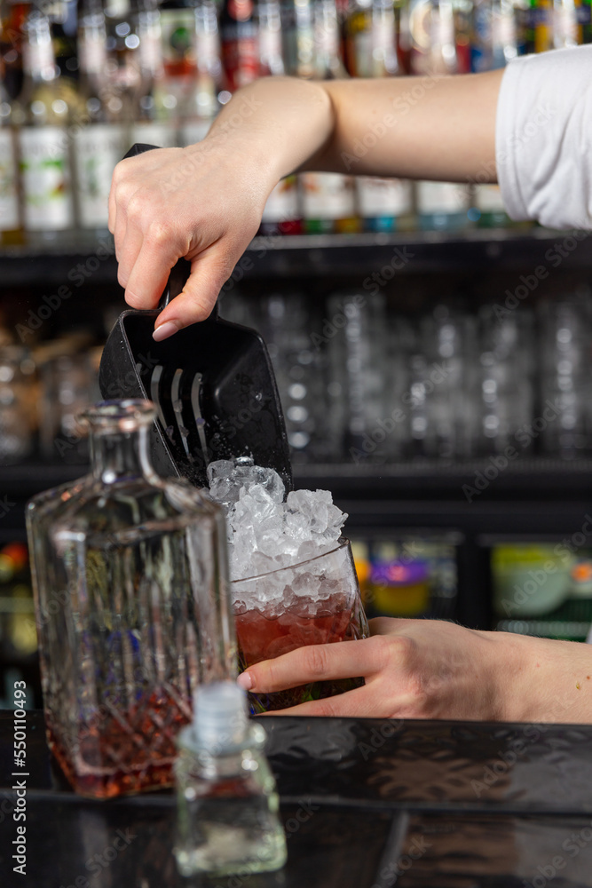 Woman bartender pouring crushed ice into glass on bar counter using a special scoop.