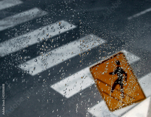 A pedestrian sign and a pedestrian crossing in front of a wet window.