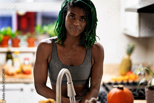 Valokuva Black woman with green dreadlocks cleaning and eating fruit in her kitchen