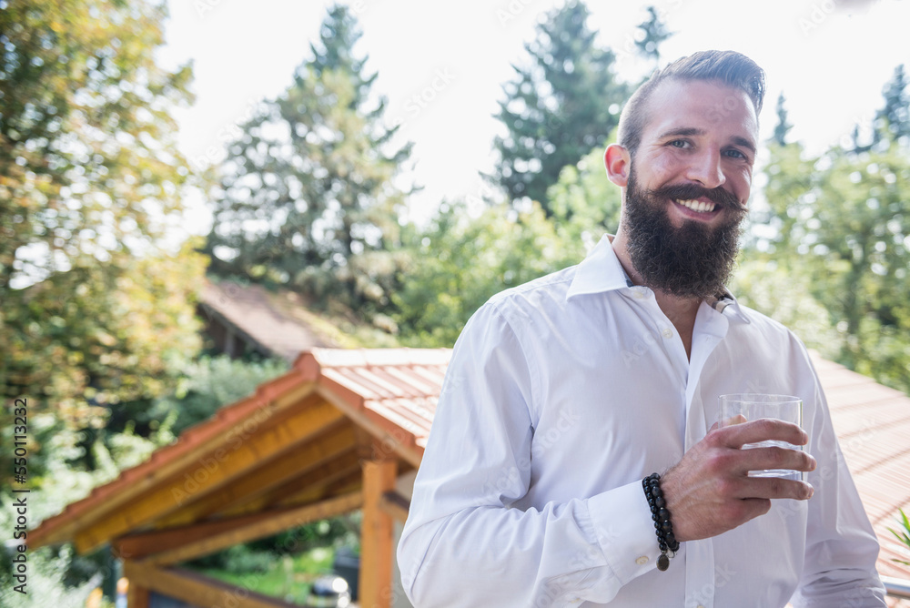Portrait of a young man drinking water on the balcony and smiling, Bavaria, Germany Portrait of a young man drinking water on the balcony and smiling, Bavaria, Germany