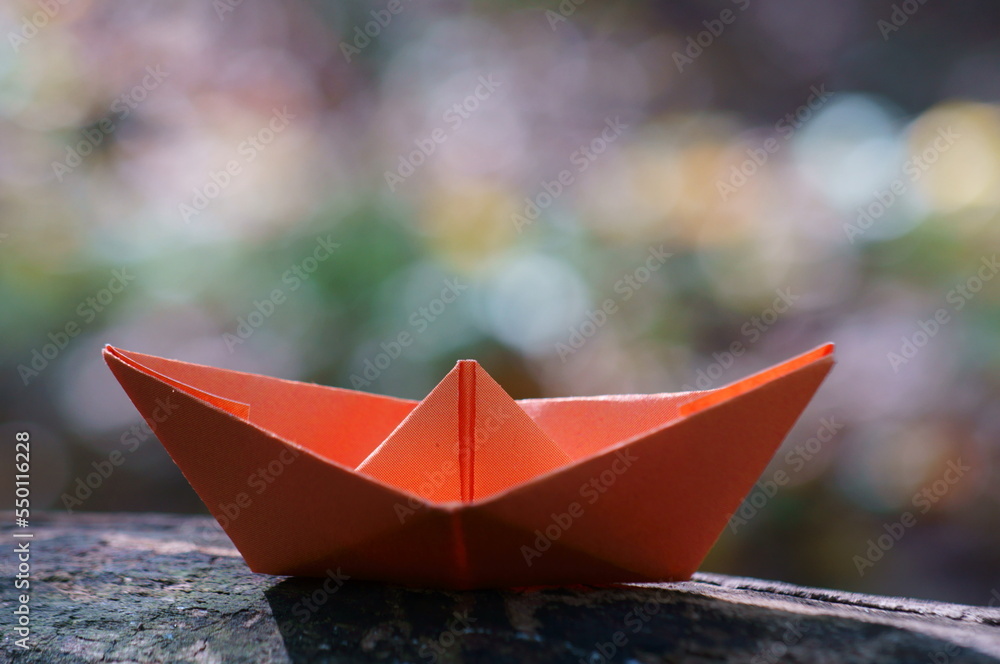 Orange paper boat on the background of autumn leaves.