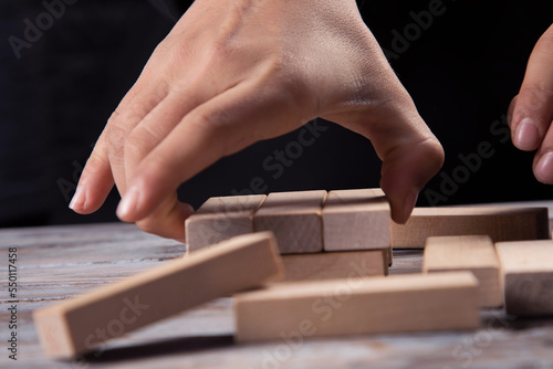 Close-up hand takes one block on a wooden block tower.