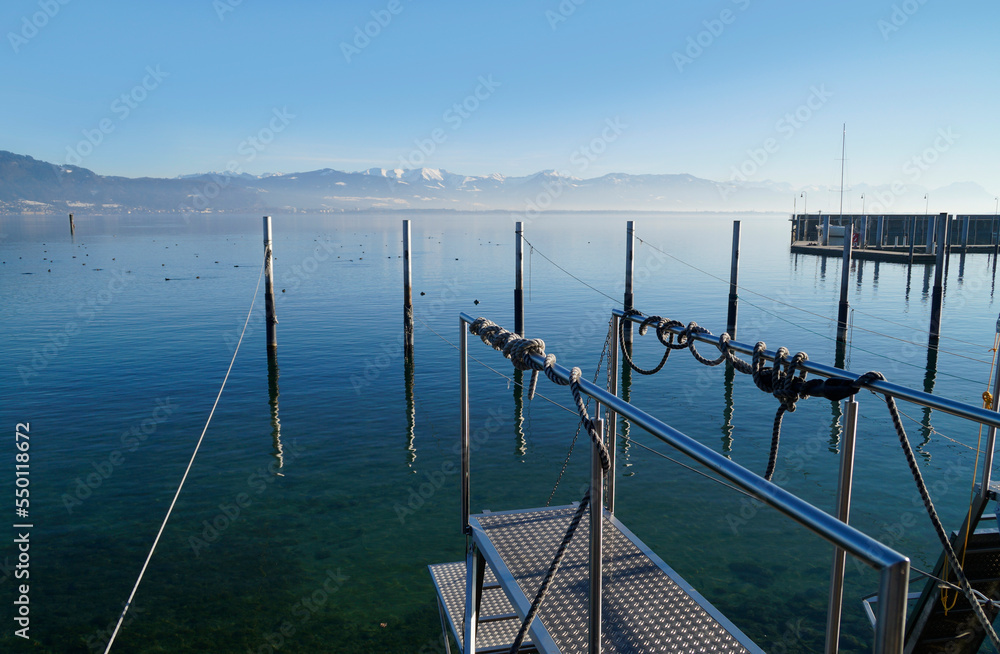 harbour of Lindau island on tranquil lake Constance or lake Bodensee with the Alps in the background on a fine winter evening with the scenic sky and white clouds reflected in the water (Germany)