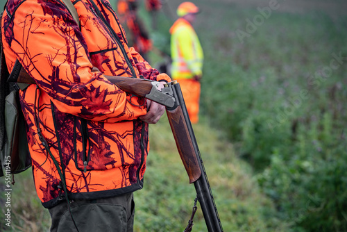 Sicherheit bei der Jagd: Jäger wartet am Feldrand mit nicht schußbereiter Waffe und in Signalkleidung.