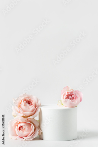 Empty white podium and pink roses on light grey background. Minimal cosmetic template. Round showcase for product marketing. Abstract display or stage. Spa and beauty concept. Still life. Copy space.