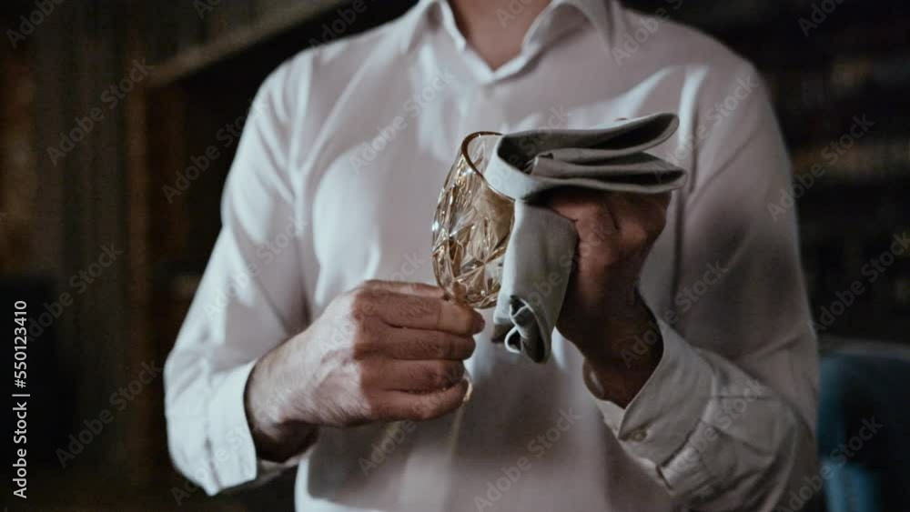 The hands of a professional waiter are wiping a glass glass with a gray cloth. The hands of a professional waiter are wiping a glass glass with a gray cloth.