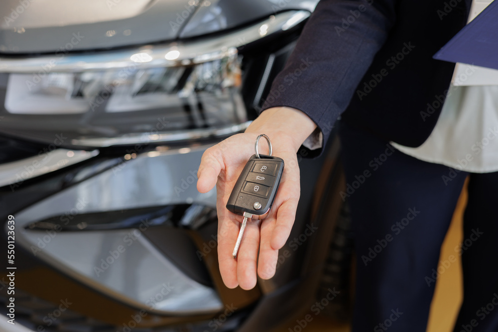 woman's hand holds the key to a new car, buying and selling at a car dealership. conclusion of a contract for the maintenance of a car, purchase on credit or trade in