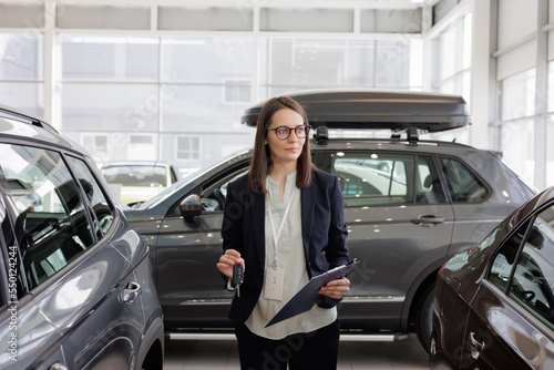 woman sells a car at a car dealership and hands over the keys to the buyer. nice woman car sales manager. a successful and happy woman with a tablet in her hands is the head of a car dealership © MyJuly