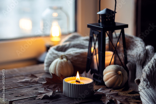 Cozy autumn composition with aromatic candle, pumpkins, wool sweater, leaves, cinnamon. Aromatherapy on a grey fall morning, home atmosphere of cosiness and relax. Wooden background close up. photo