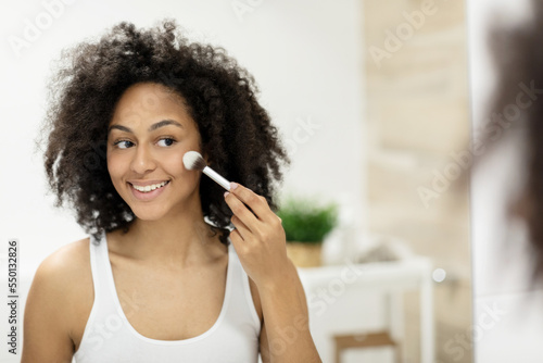 Happy woman in white tank top outlines face while holding makeup brush