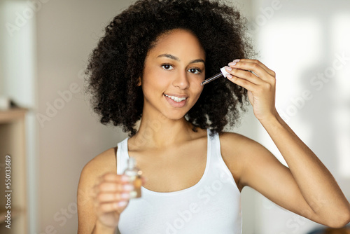 Face Skincare. Happy Woman Applying Facial Serum With Dropper Moisturizing Skin Smiling To Camera Standing Posing In Bathroom At Home. Domestic Skin Care Routine Concept. Beauty And Cosmetics