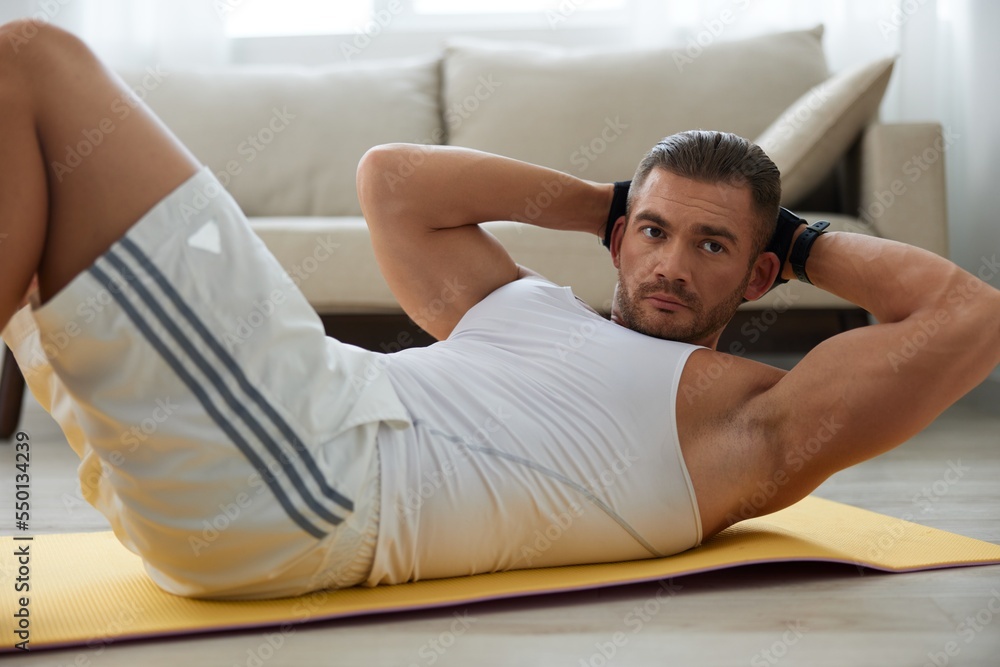 Obraz premium Man sports home training on the floor on a mat with dumbbells, exercises for muscle growth, pumped up man fitness trainer exercises at home, the concept of health and beauty of the body