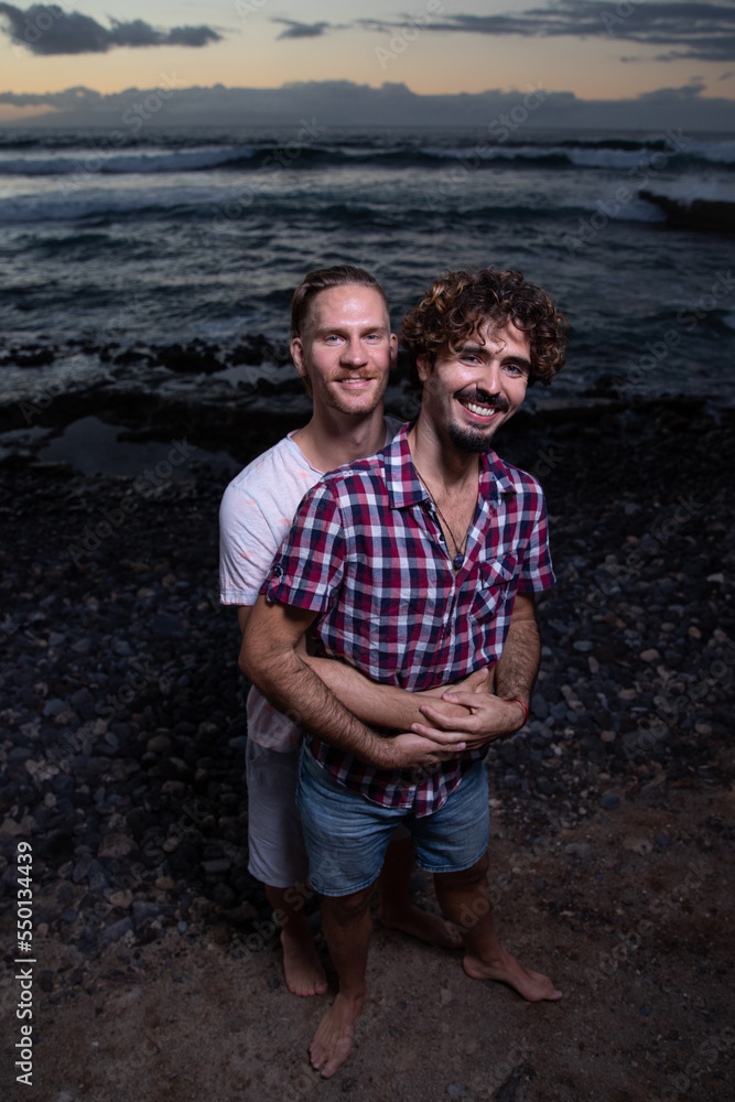 Gay boyfriends hugging at the beach enjoying their holidays during the sunset.
