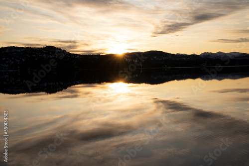 Dramatic sunrise. View of the sun hiding in the horizon and beautiful daybreak sky with clouds reflection in the lake s water surface.  