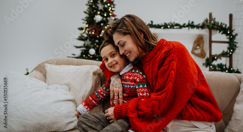 Young mother with dark hair embracing with her son near Christmas tree in room decorated for holiday © Big Shot Theory