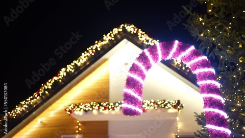 Christmas candy made from garland and glowing lights standing in front the beutifully decorated house. Slow motion.  photo