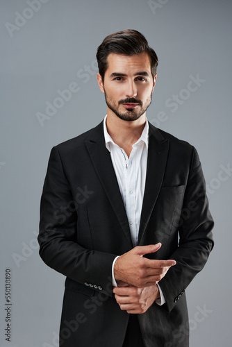 A man in a business suit businessman poses against a gray background straightening his tie and looking at the camera