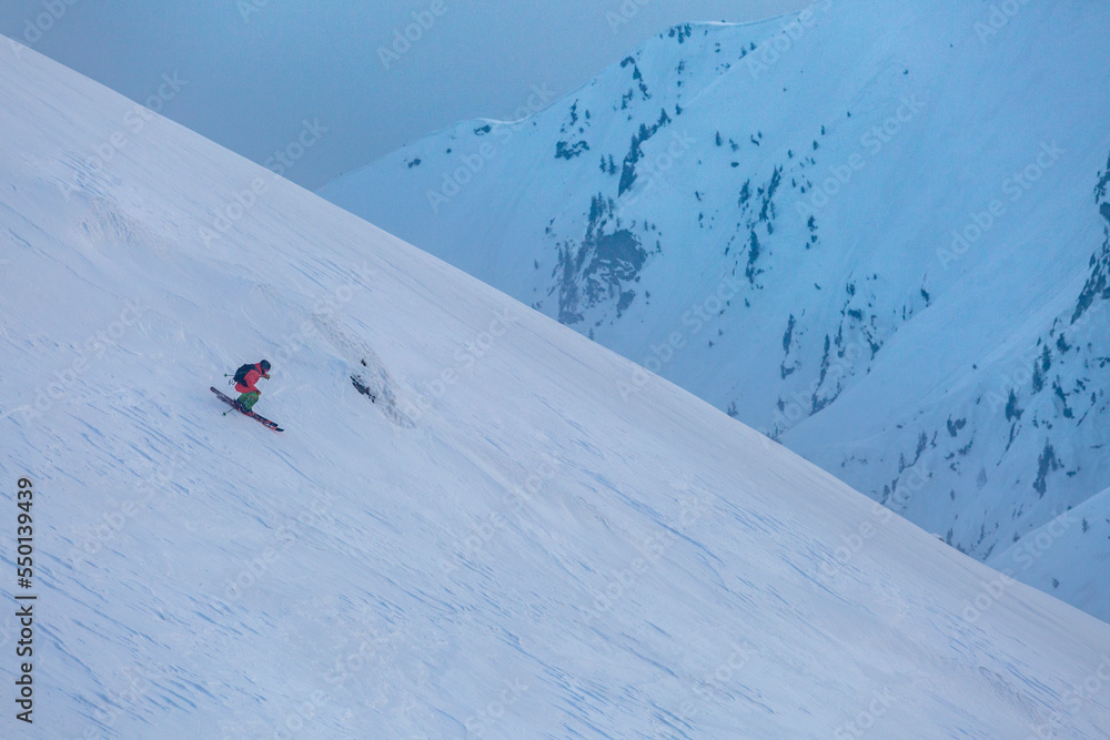 A skier descends a difficult freeride route among rocks and trees