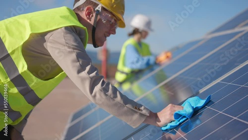 Two inspectors closeup in protective vest and helmets clean solar panels. Man woman engineers builders wipe surface of solar panel. Effiency Problem. Energetics, engineering modern technology concept photo