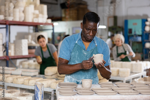 Portrait of african american worker cutting burrs off freshly made earthenware cups and plates with a knife