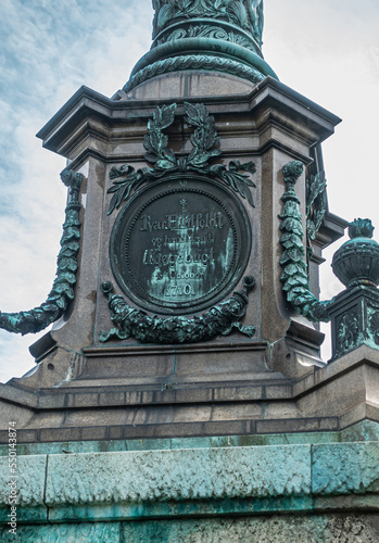 Copenhagen, Denmark - July 24, 2022: Ivar Huitfeldt Column detail. Bronze mural statue at bottom of Admirals brown stone column in Langelinie Park under blue cloudscape photo