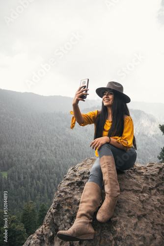 Young woman taking self portrait with her cell phone in a forest landscape, vertical